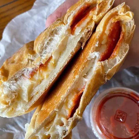 A pepperoni pizza bread torn in half over paper, with a cup of marinara